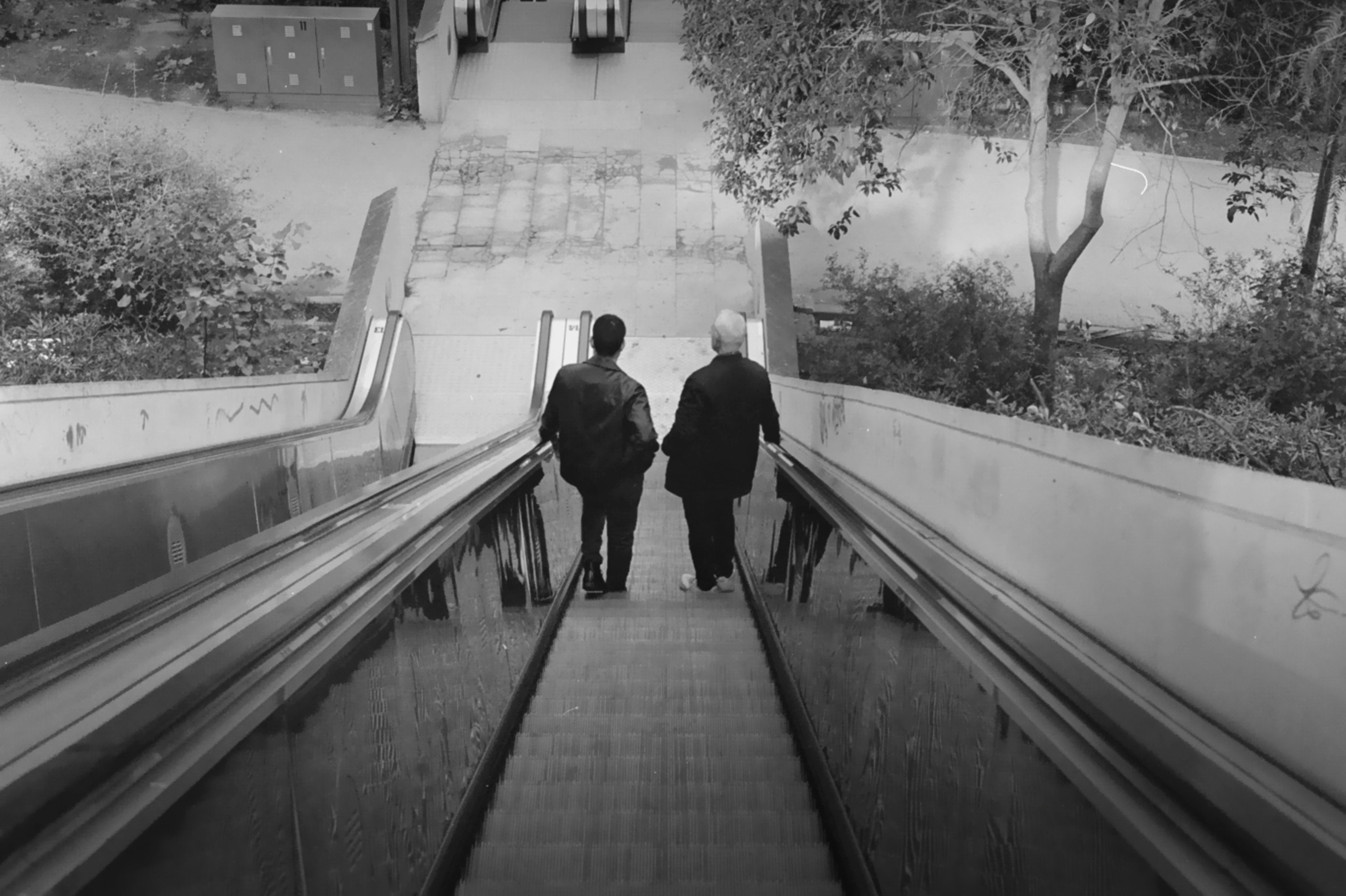 Two people descend an escalator.