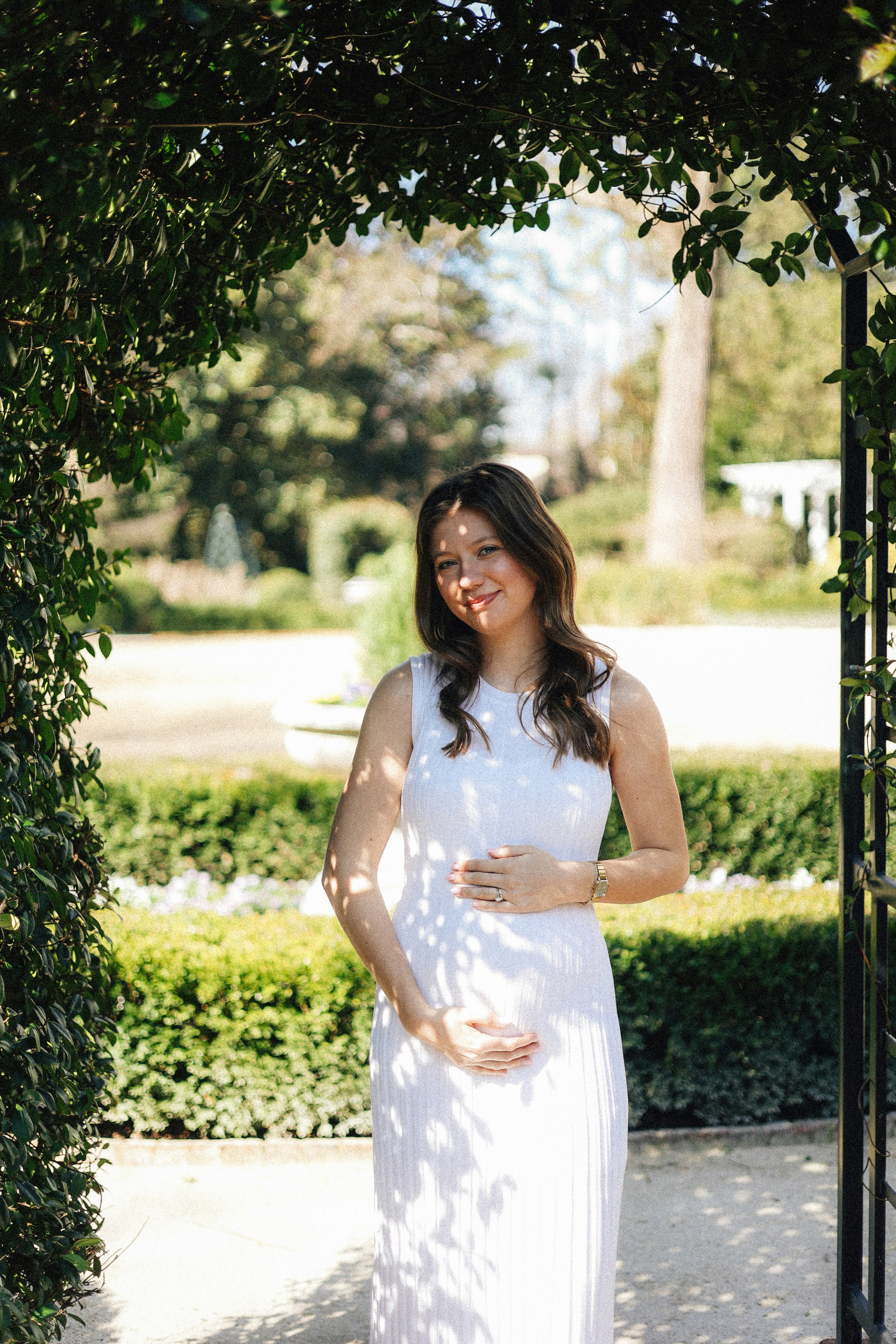 Pregnant woman poses in a garden archway.