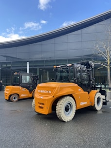 Orange forklifts parked outside a modern building.