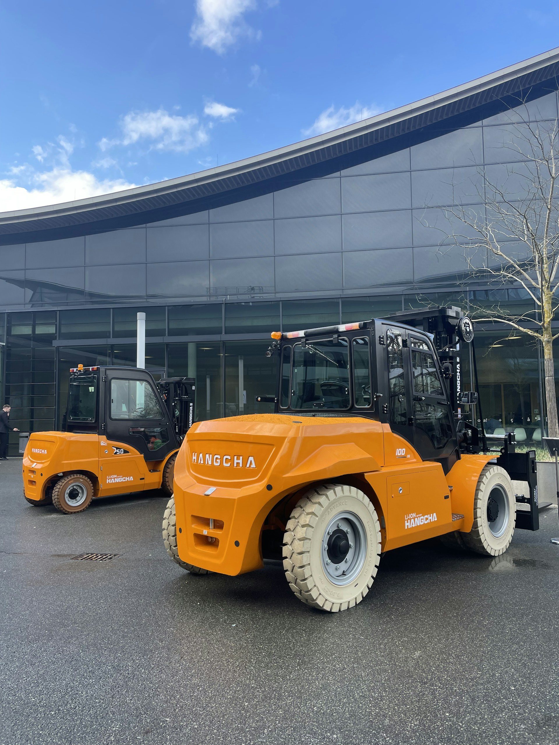 Orange forklifts parked outside a modern building.