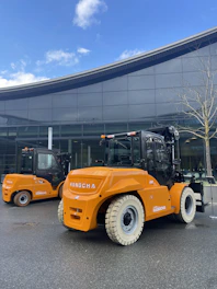 Two orange forklifts are parked in front of a building.