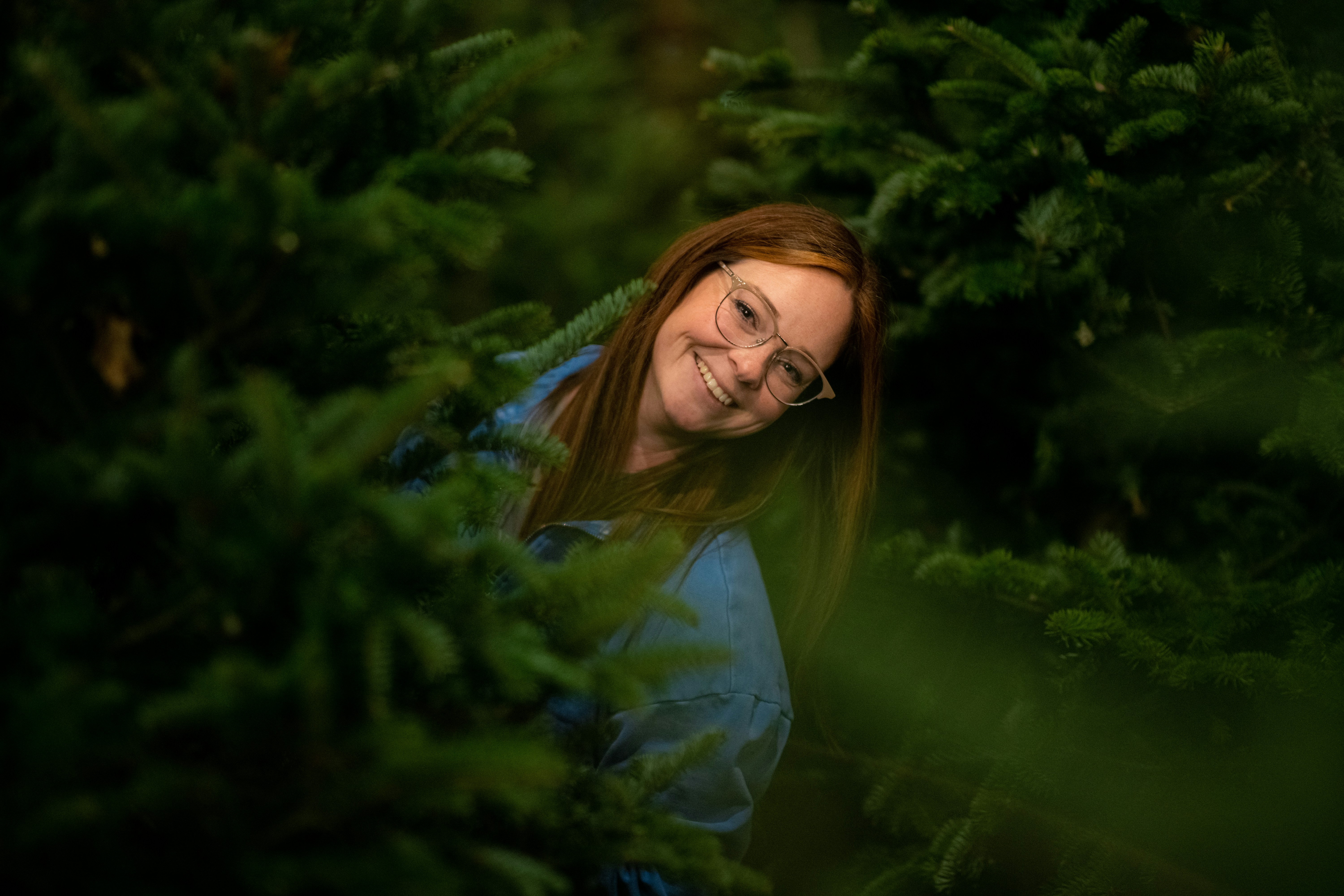 A woman smiles from behind green foliage.