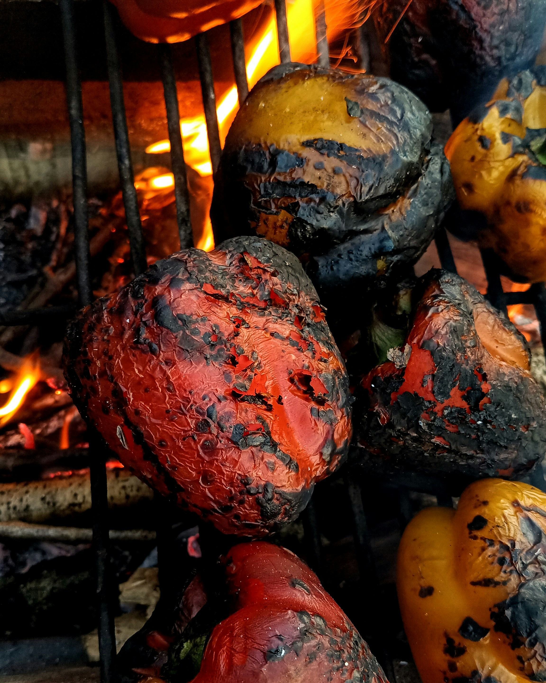 Charred red and yellow peppers on grill grates with visible blackened skin`