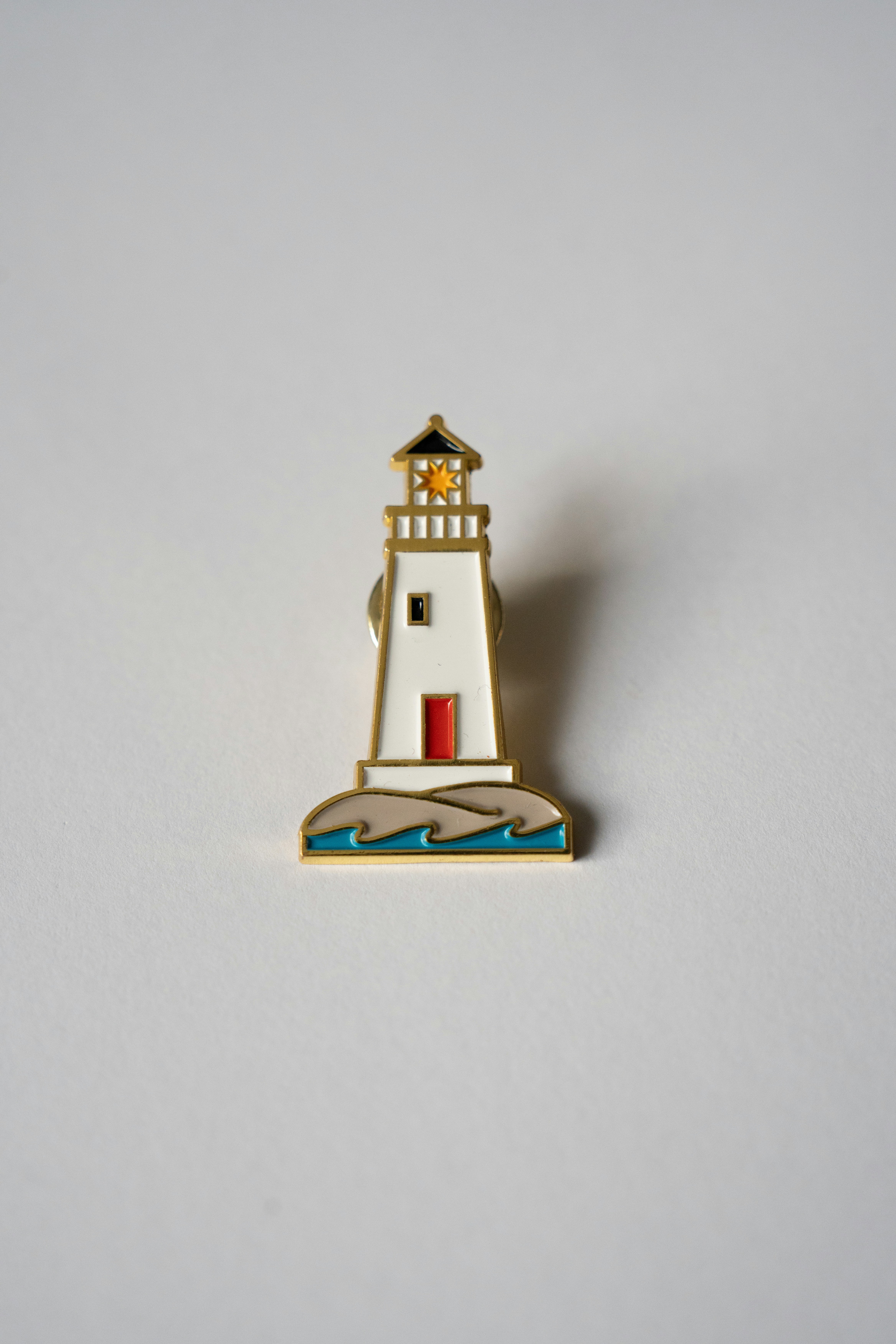 A lighthouse pin is displayed on a white surface.