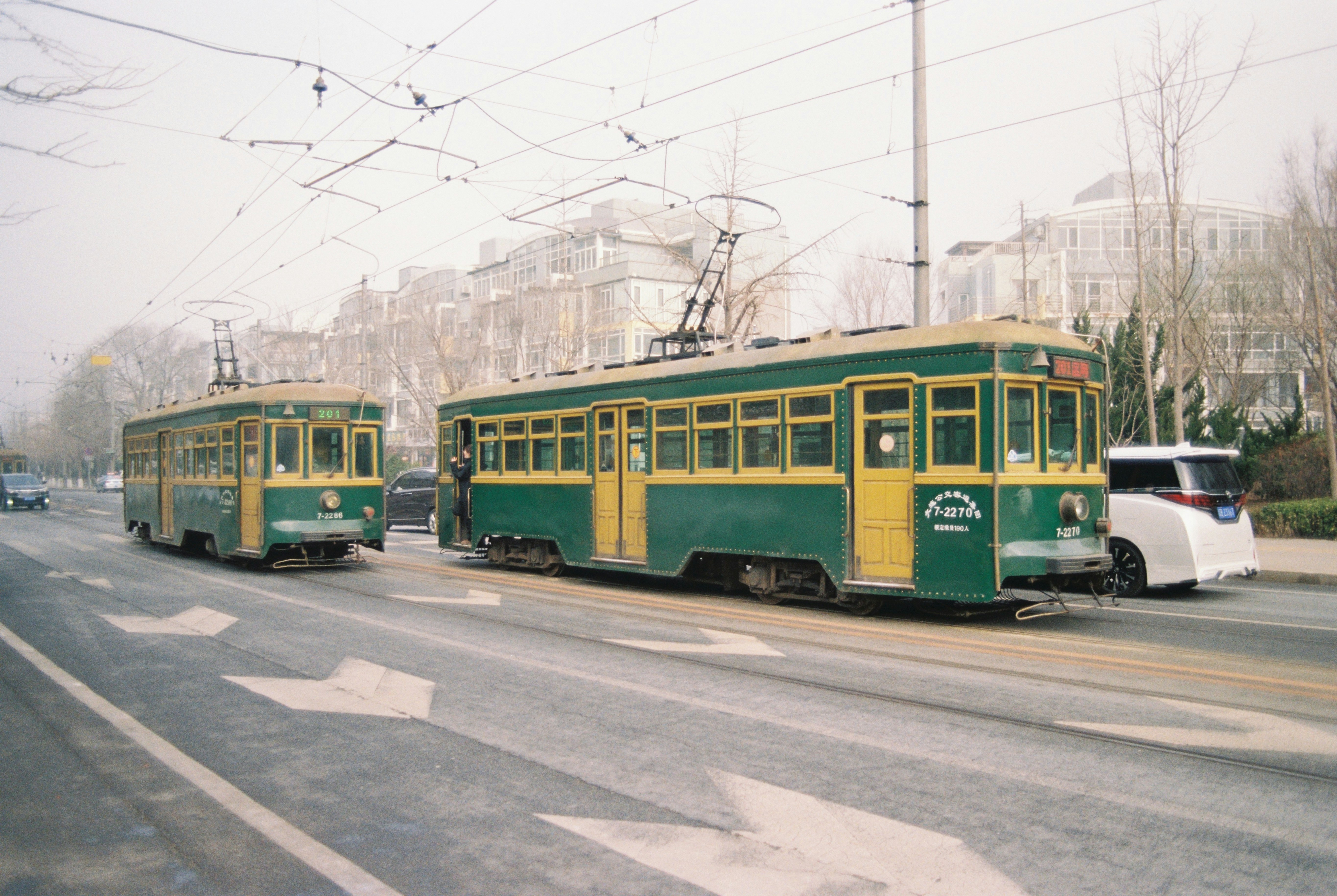 Vintage green trams travel down a city street.