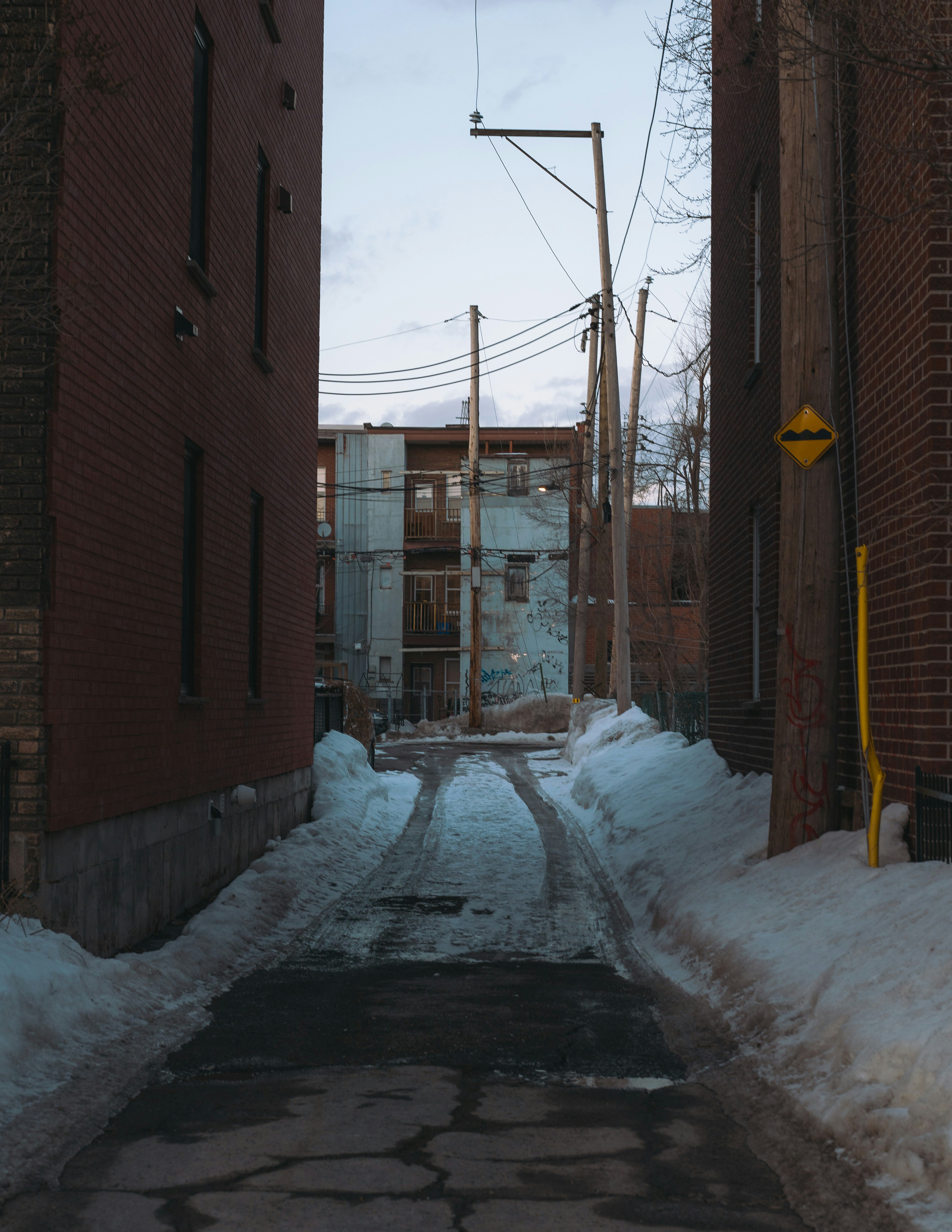 Snowy alleyway between brick buildings at dusk.