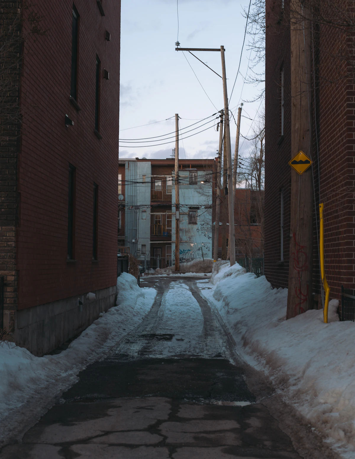 Snow-dusted brick alleyway at dusk evoking the quiet of a New England mill town in winter