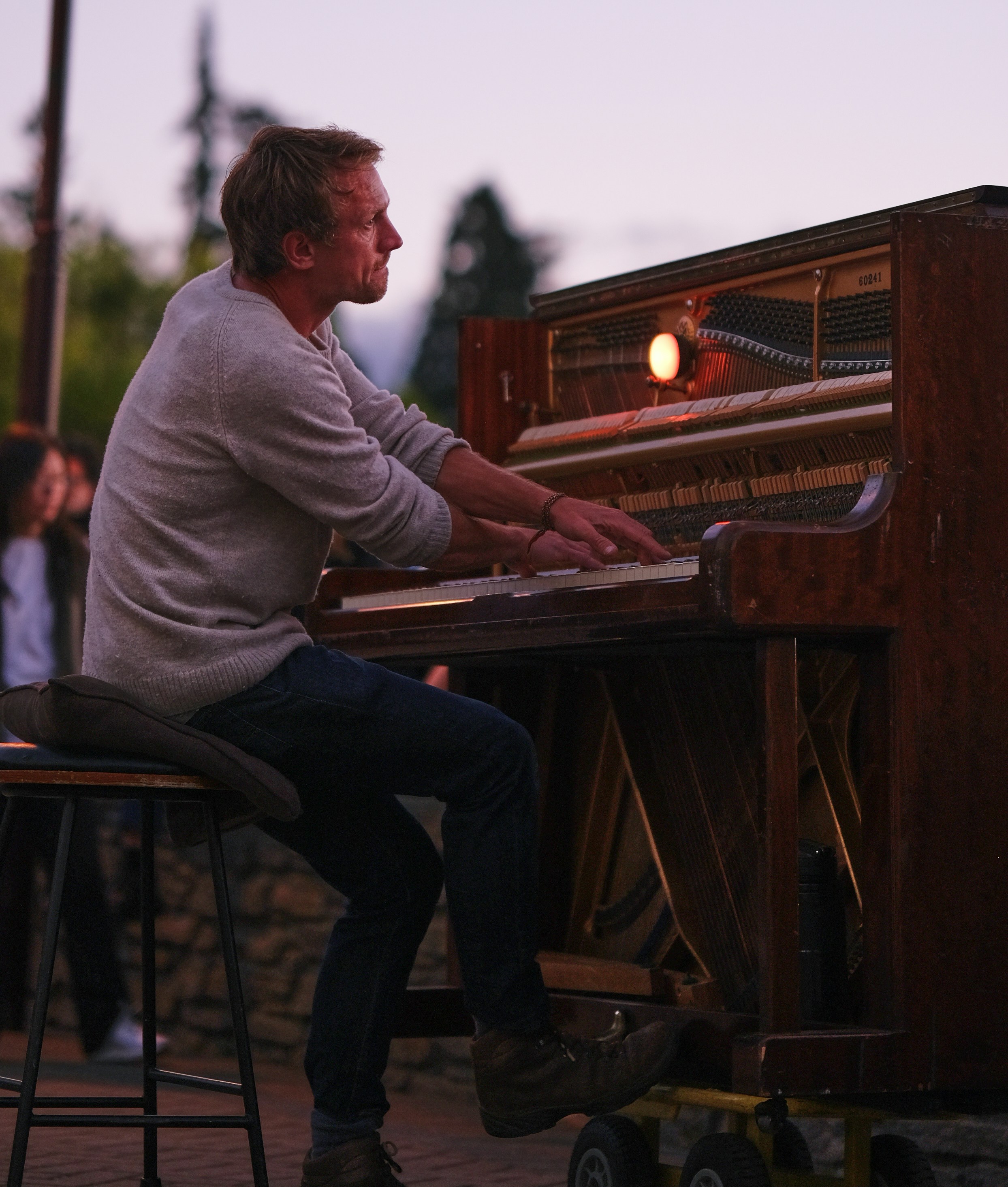 A man plays piano outdoors at dusk.
