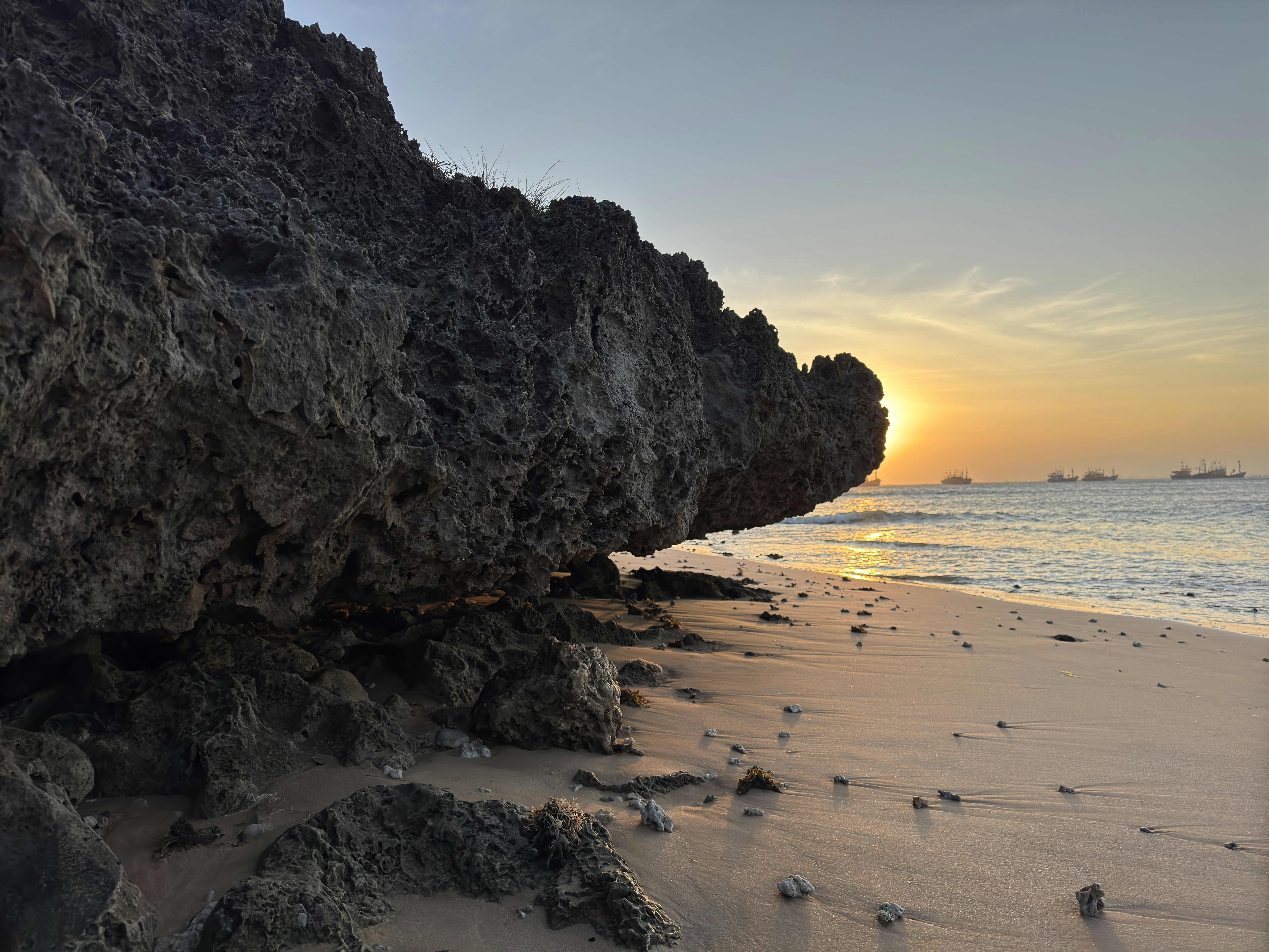 Sunset illuminates the beach and rocky cliff.