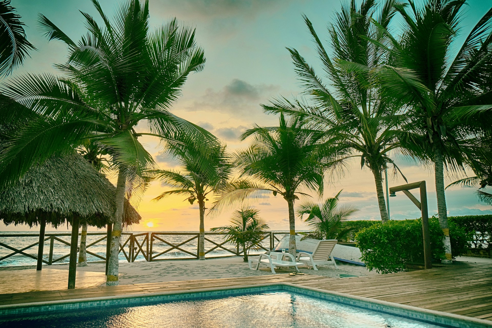 Sunset over ocean palm trees and a pool.