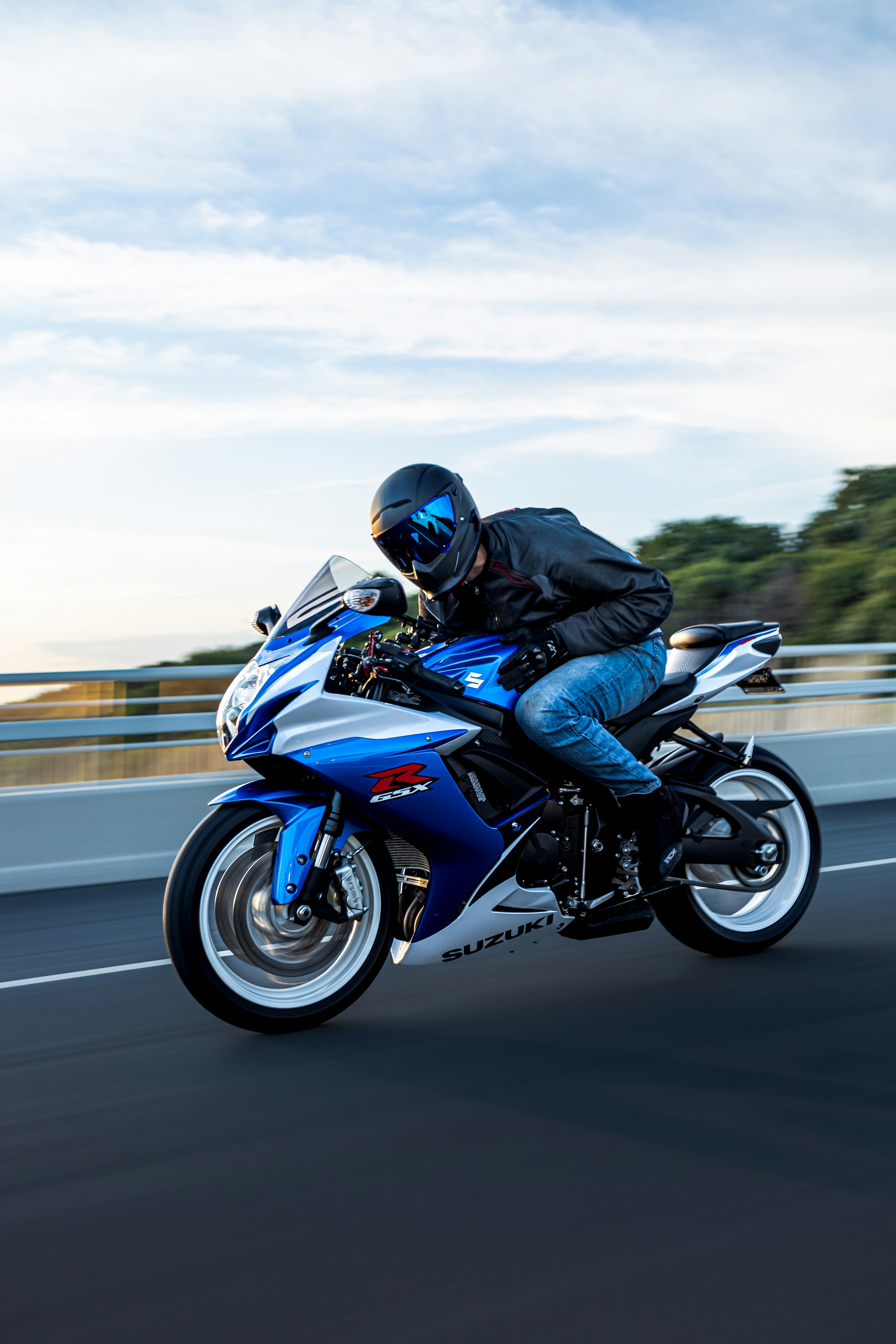 A man rides a blue and white suzuki motorcycle.