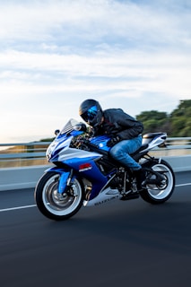 A man rides a blue and white suzuki motorcycle.