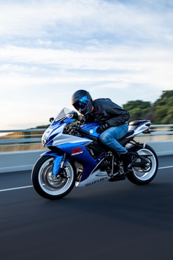 A man rides a blue and white suzuki motorcycle.