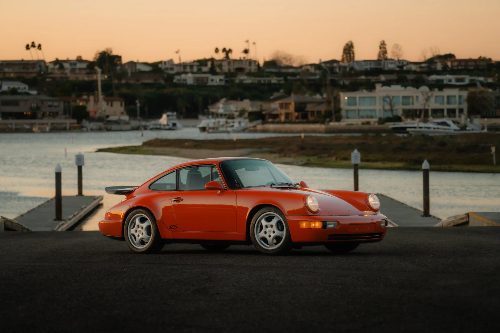 Orange classic Porsche 911 parked by a marina at sunset