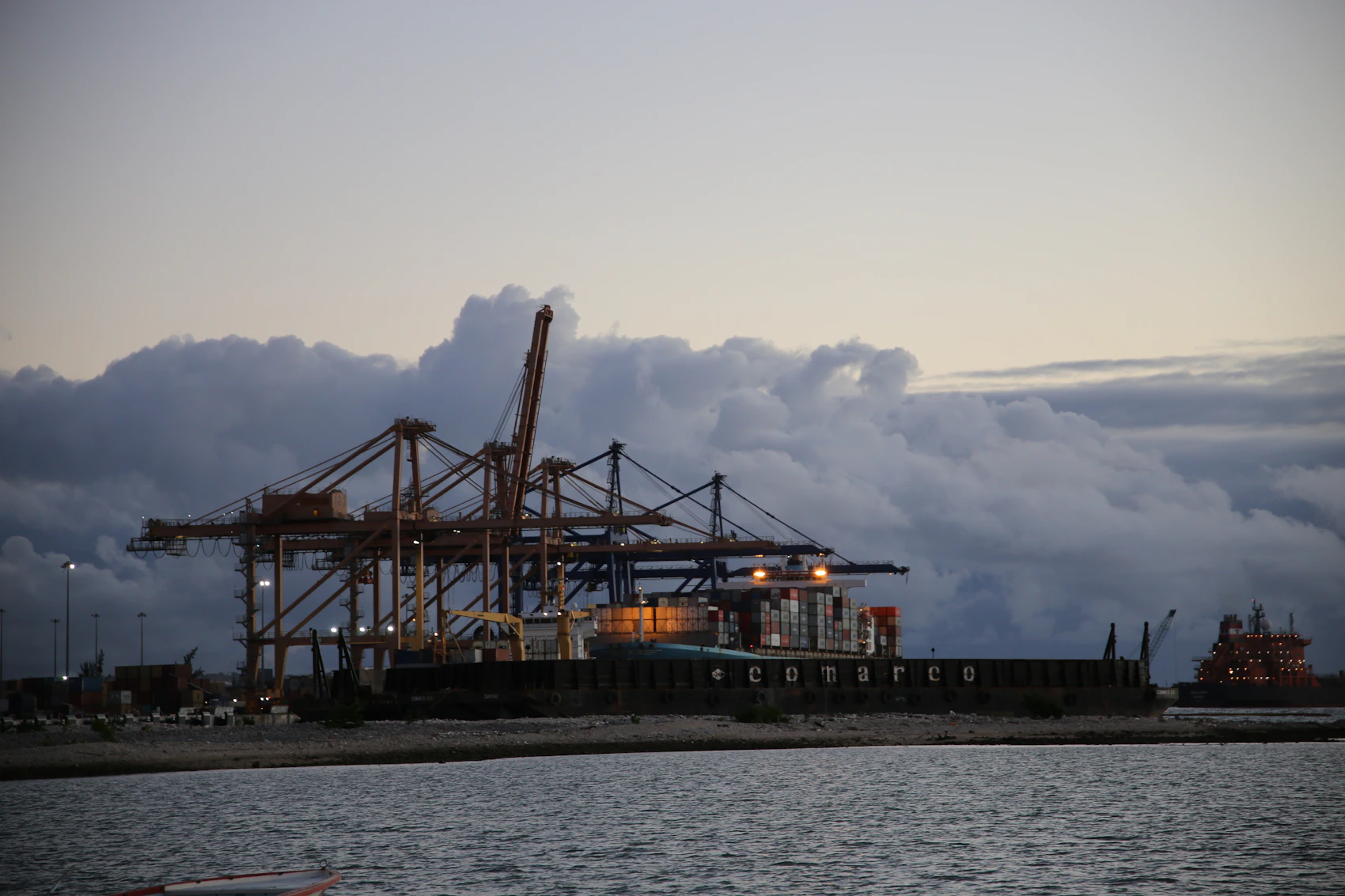 Container cranes and a cargo vessel at the working port of Port Louis beneath storm clouds