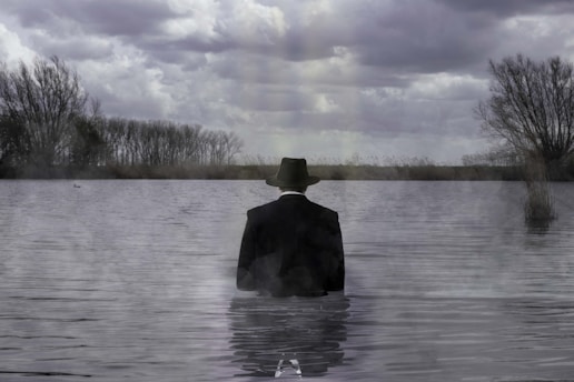 Man stands in water under a cloudy sky.