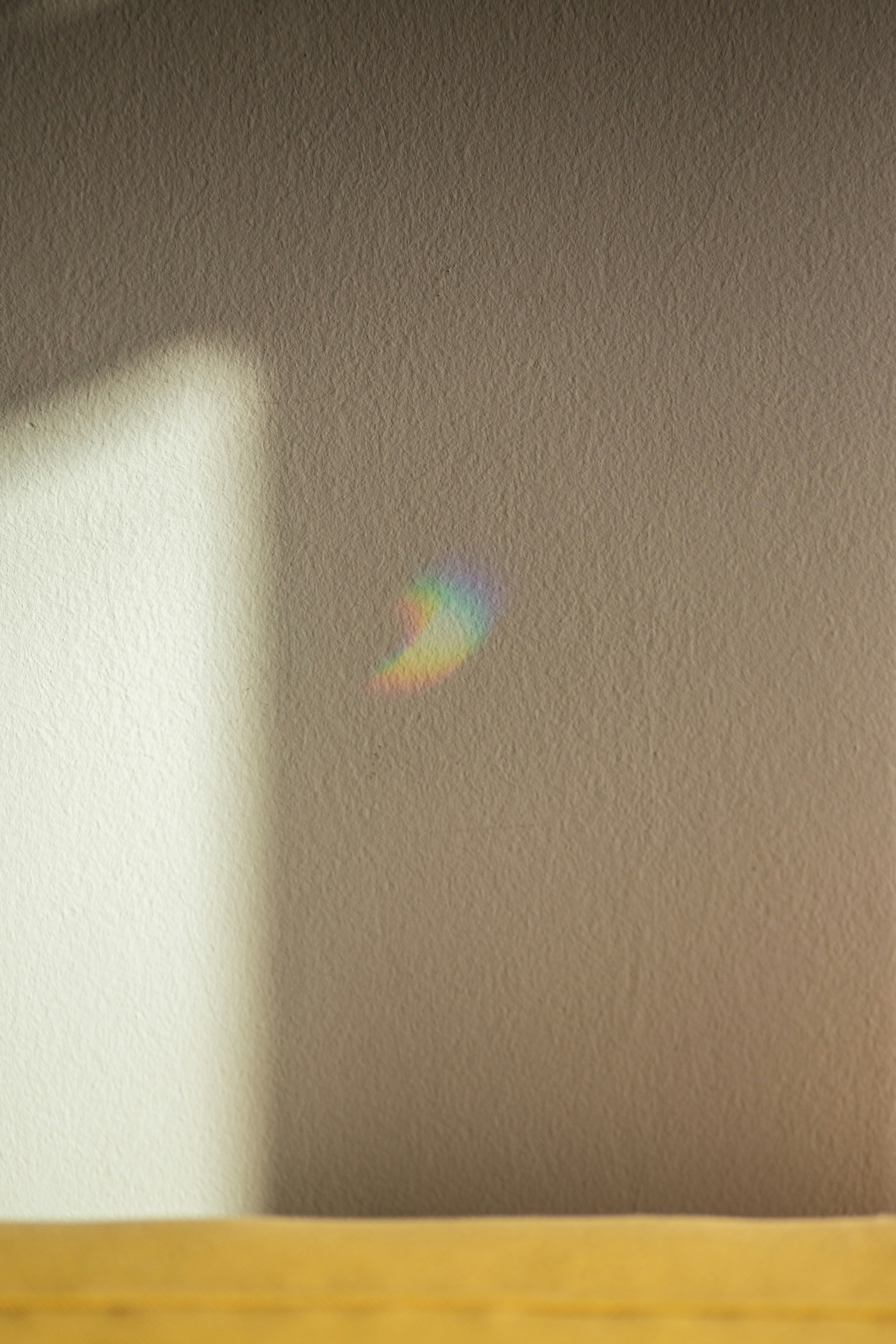 A small rainbow shines on a textured wall.