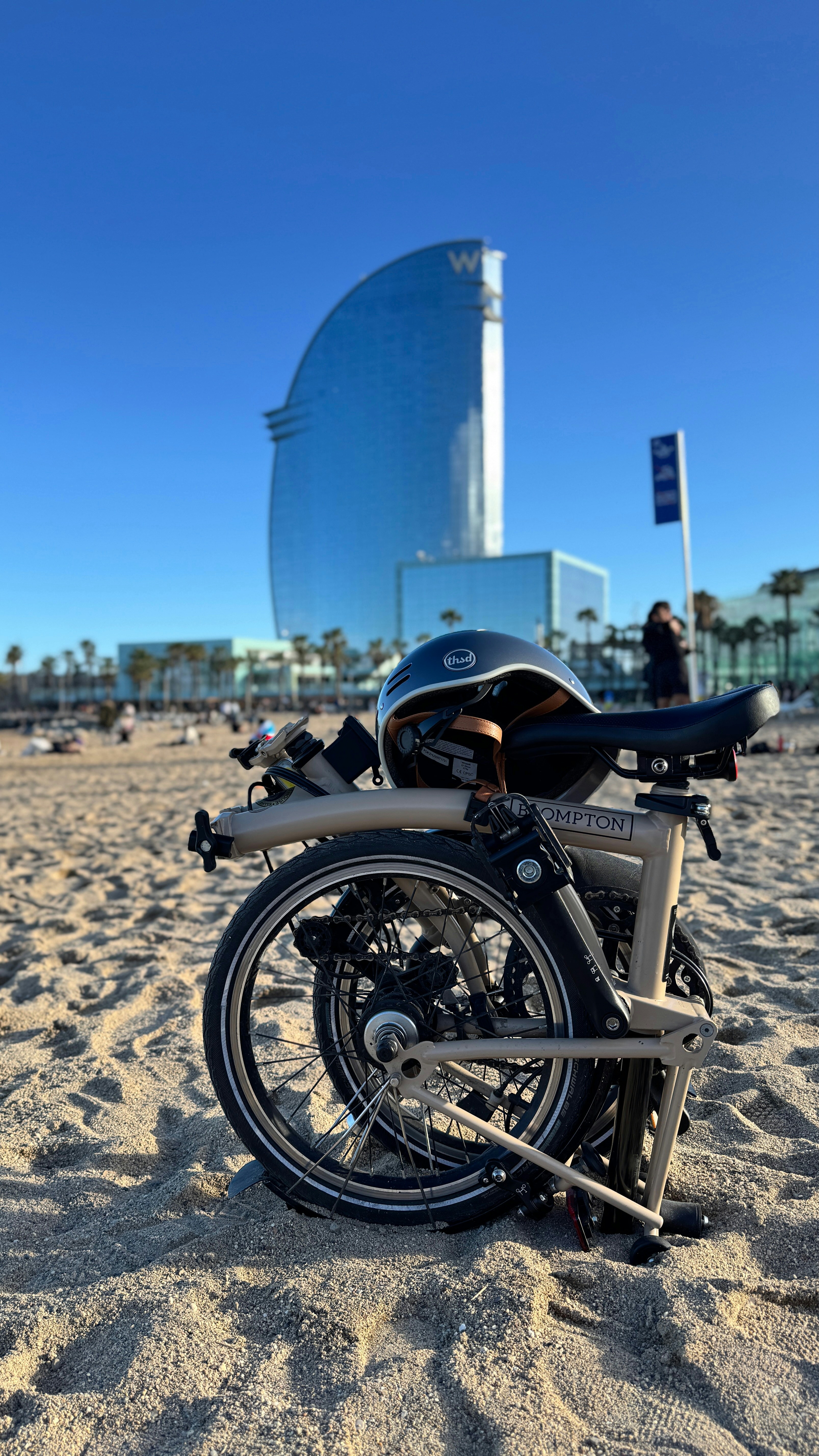 Folded bike on beach, modern building in background.