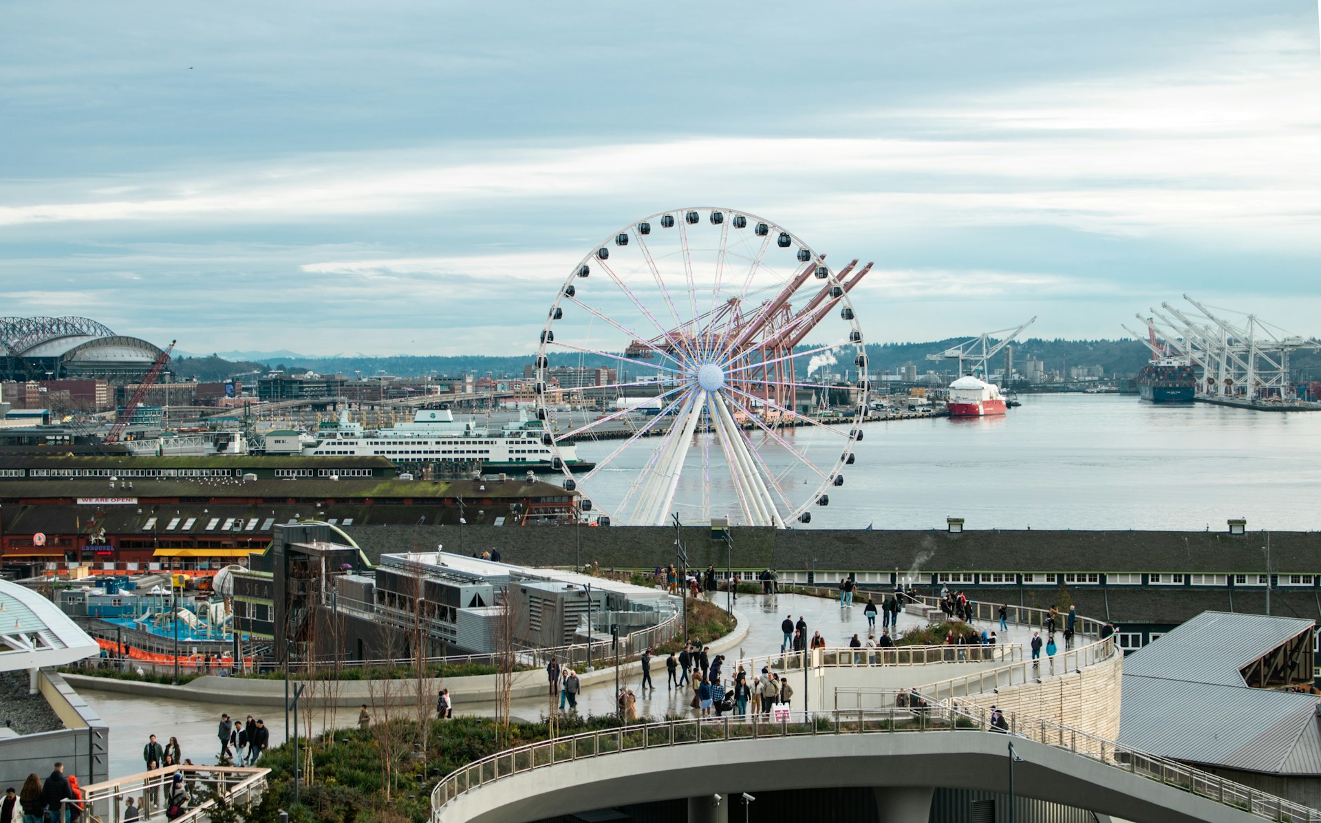 A ferris wheel overlooks a bustling harbor city.