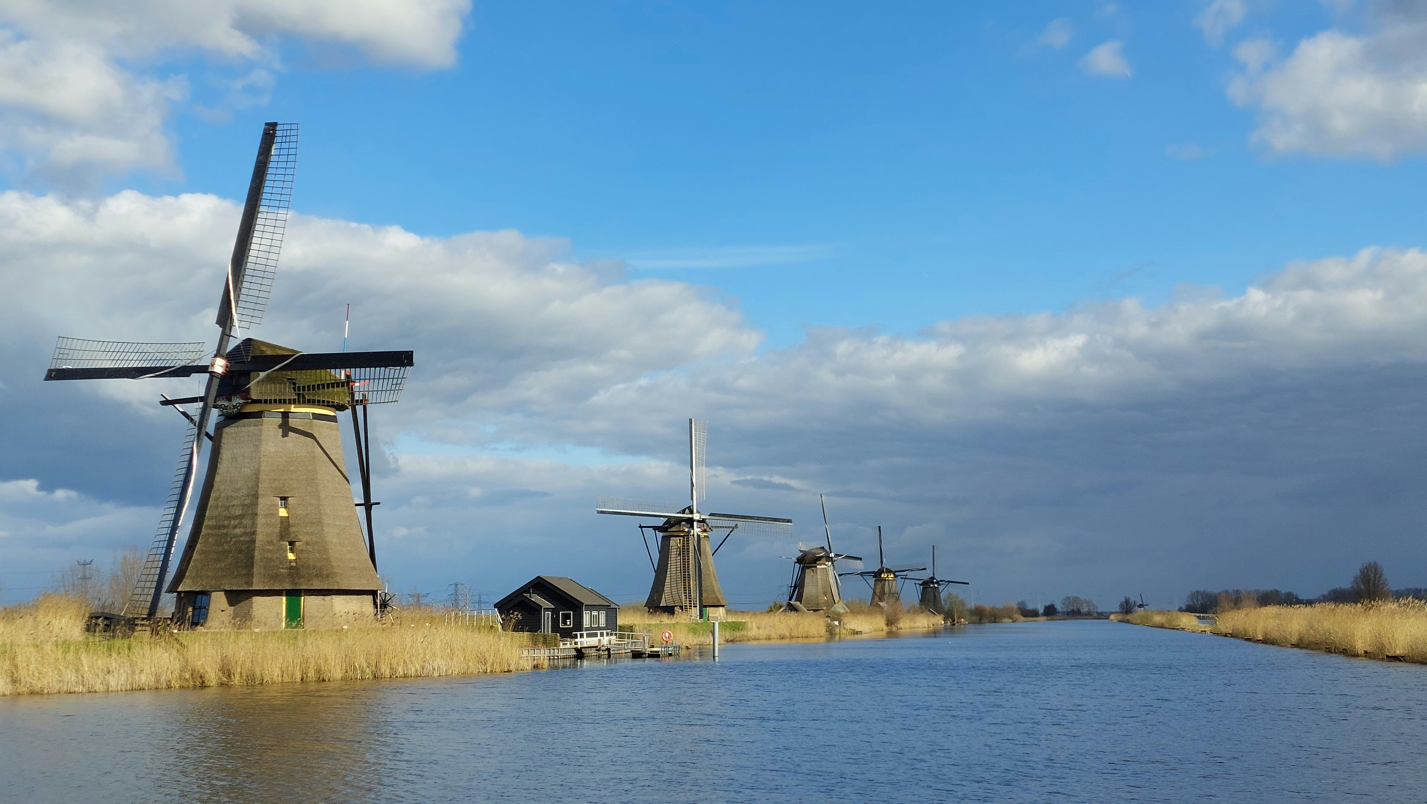 Windmills stand along a canal under a blue sky.