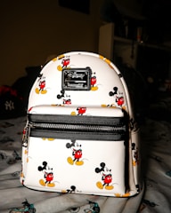 A mickey mouse backpack sits on a bed.