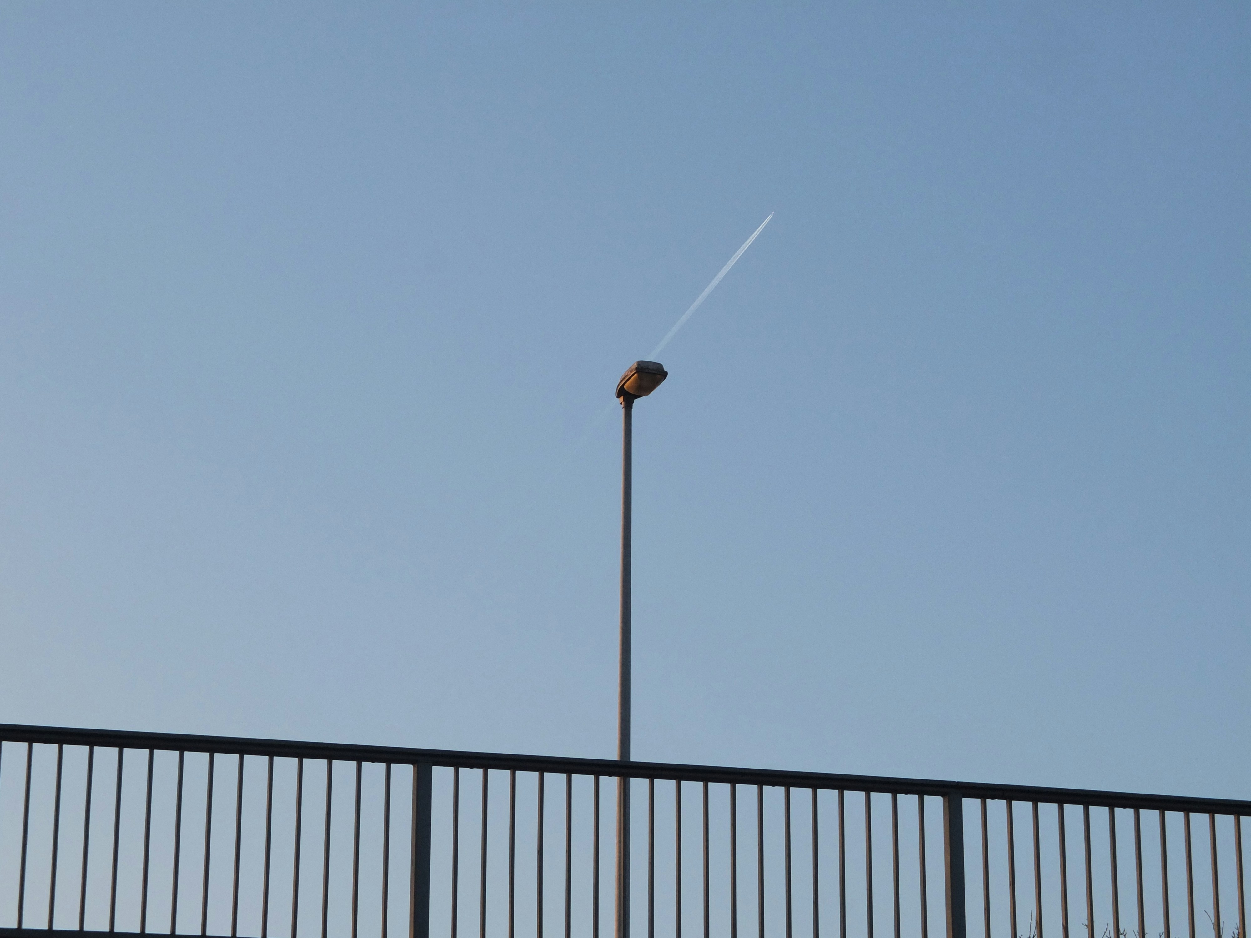 Lamp post stands with a plane's contrail in the sky.