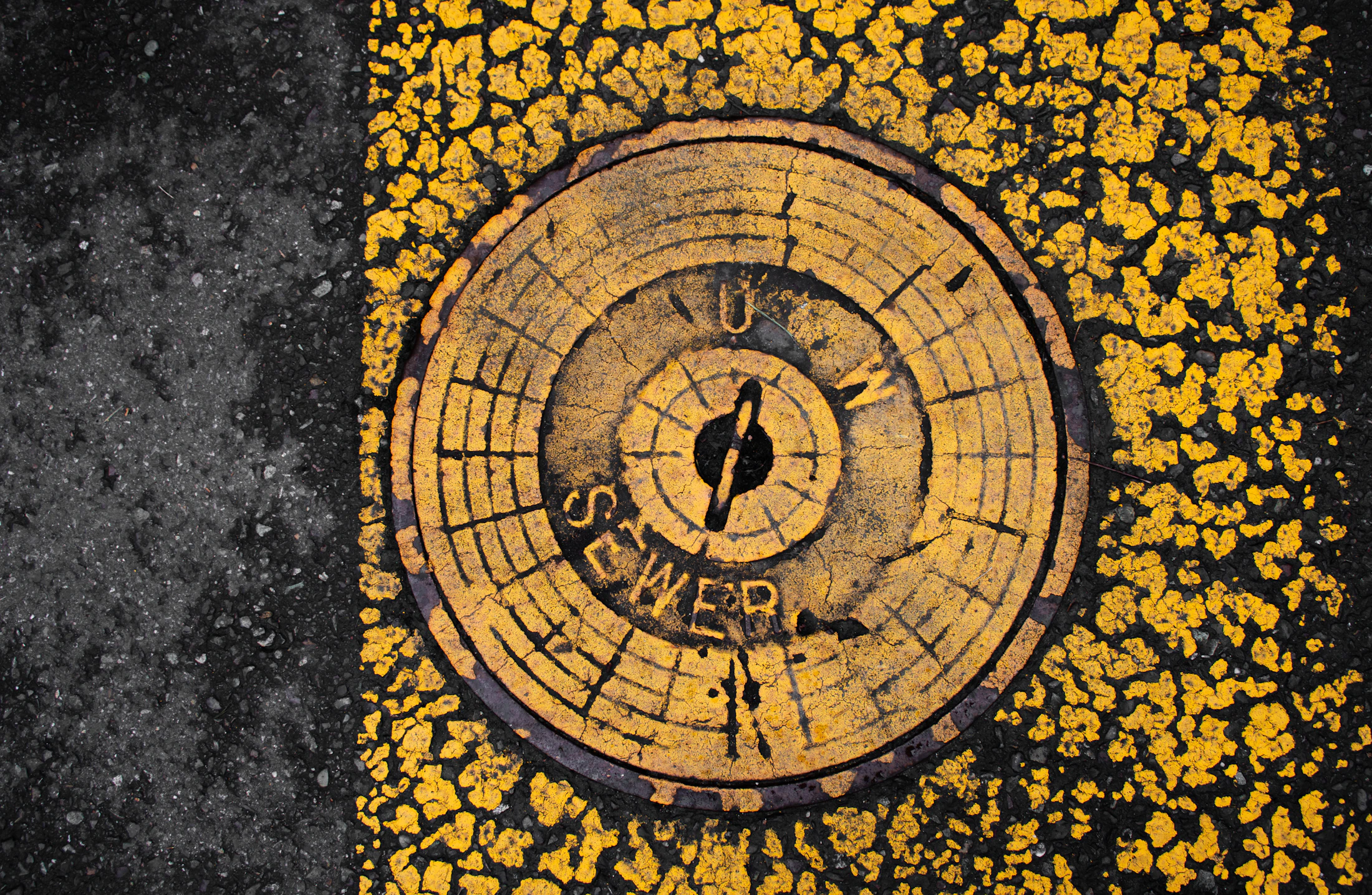 Weathered yellow sewer cover set into black pavement