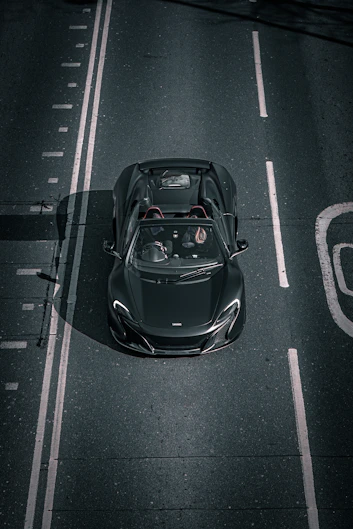 A dark convertible car is driving on the road.