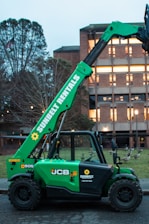 A green forklift is parked outside a building.
