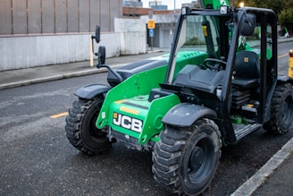 A green jcb forklift sits parked on the street.