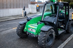 A green jcb forklift sits parked on the street.
