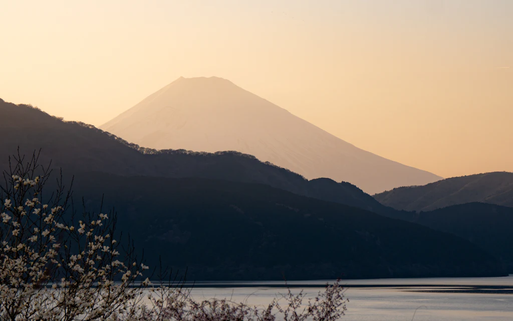 Snow-capped Mount Fuji rising beyond dark ridges and Lake Ashi at sunset