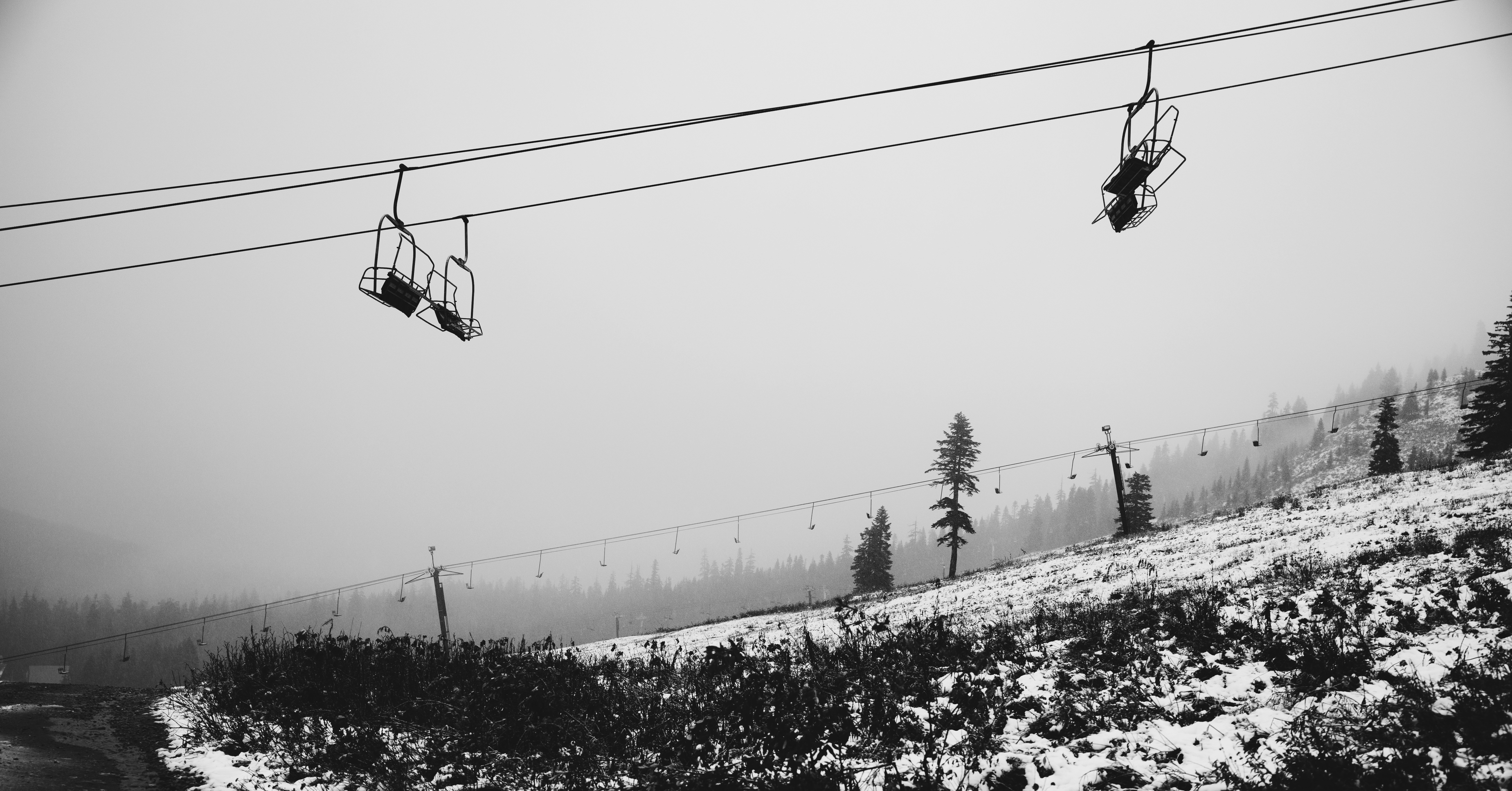 スキーリフトの椅子は、雪に覆われた曇りの山にぶら下がっています。