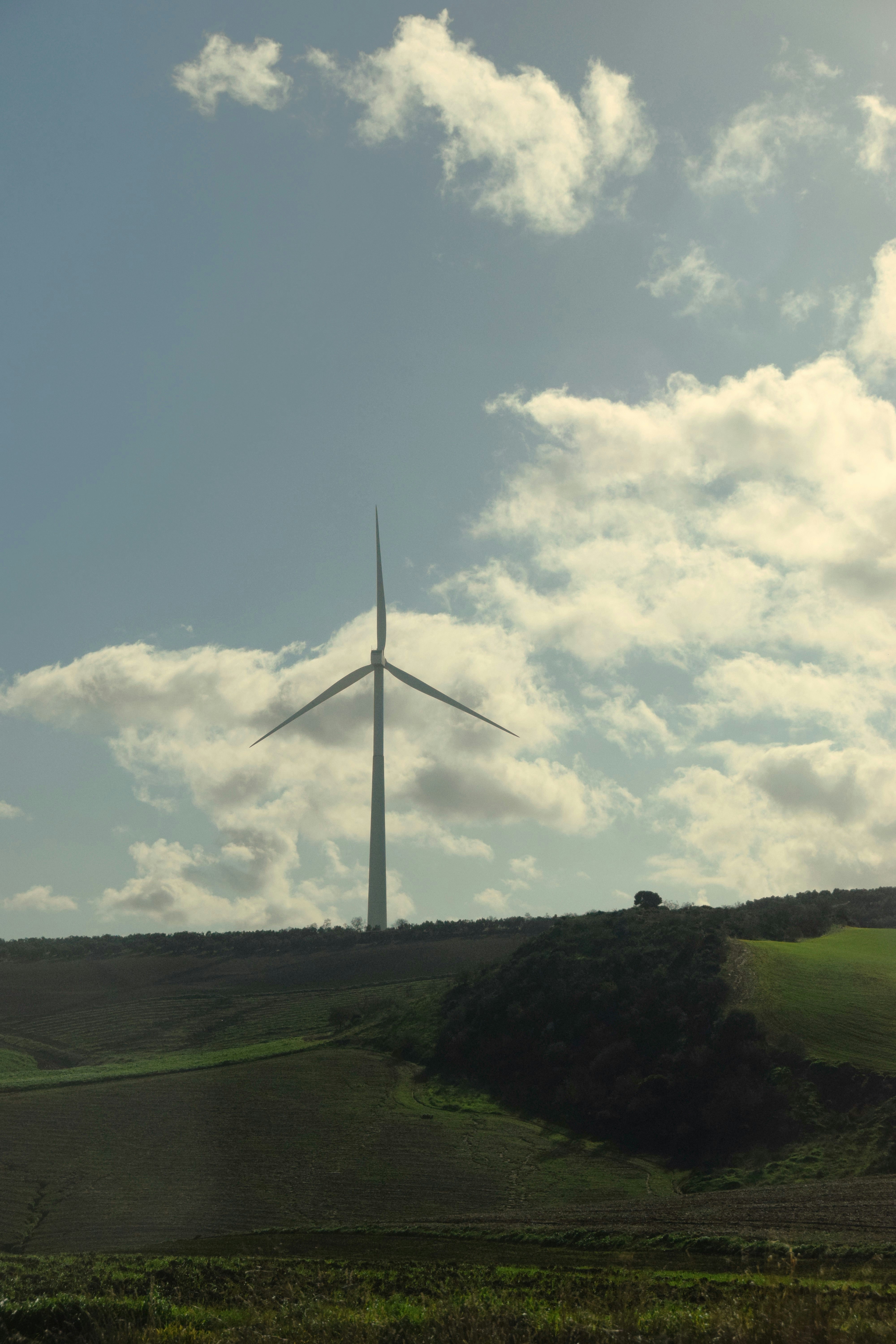 Wind turbine stands on a grassy hillside under the clouds.