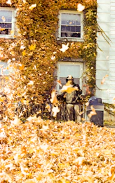 Person raking leaves in front of a building during autumn.