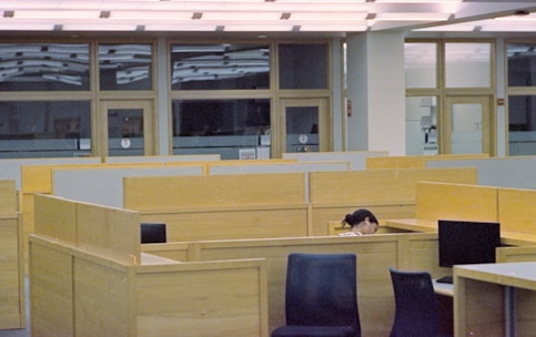 Person sleeping at a desk in a library cubicle.