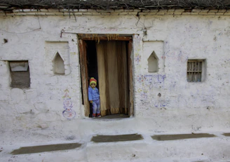 A child peeks from inside an old doorway.