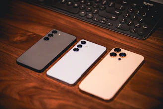 Three smartphones are on a wooden surface.