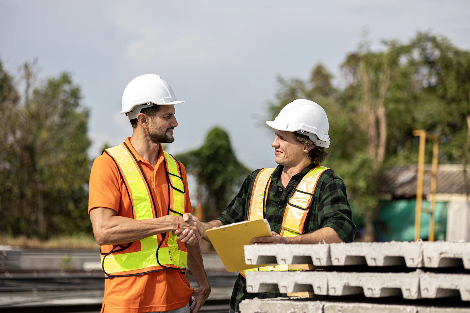 Two contractors in hard hats shaking hands over a clipboard at a jobsite
