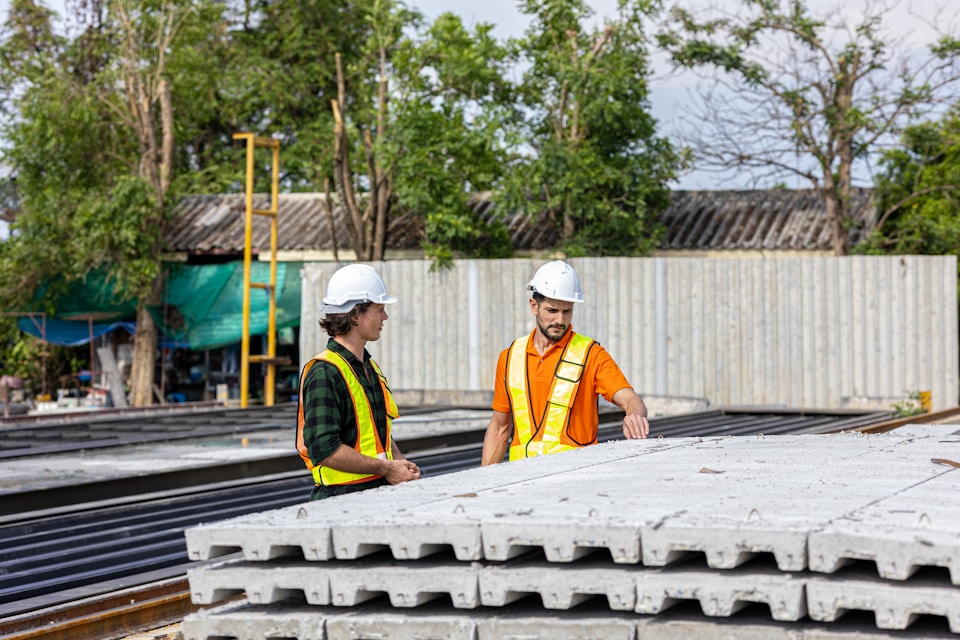 Construction workers inspect precast concrete slabs outdoors.