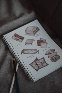 Pillow sketches fill a notebook on a gray surface.