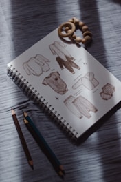Sketchbook with baby clothes illustrations and crayons.
