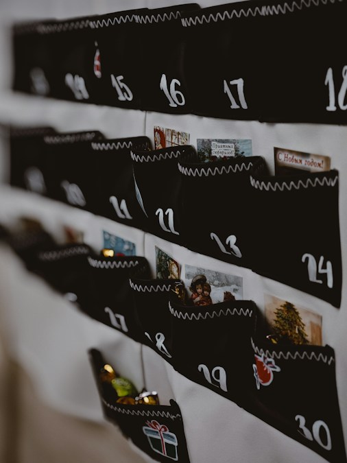 Un calendrier de l’Avent en tissu noir, aux poches numérotées 11 à 24, accroché au mur à côté de cartes de vœux