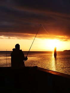 Fisherman casts into the ocean during a sunset.