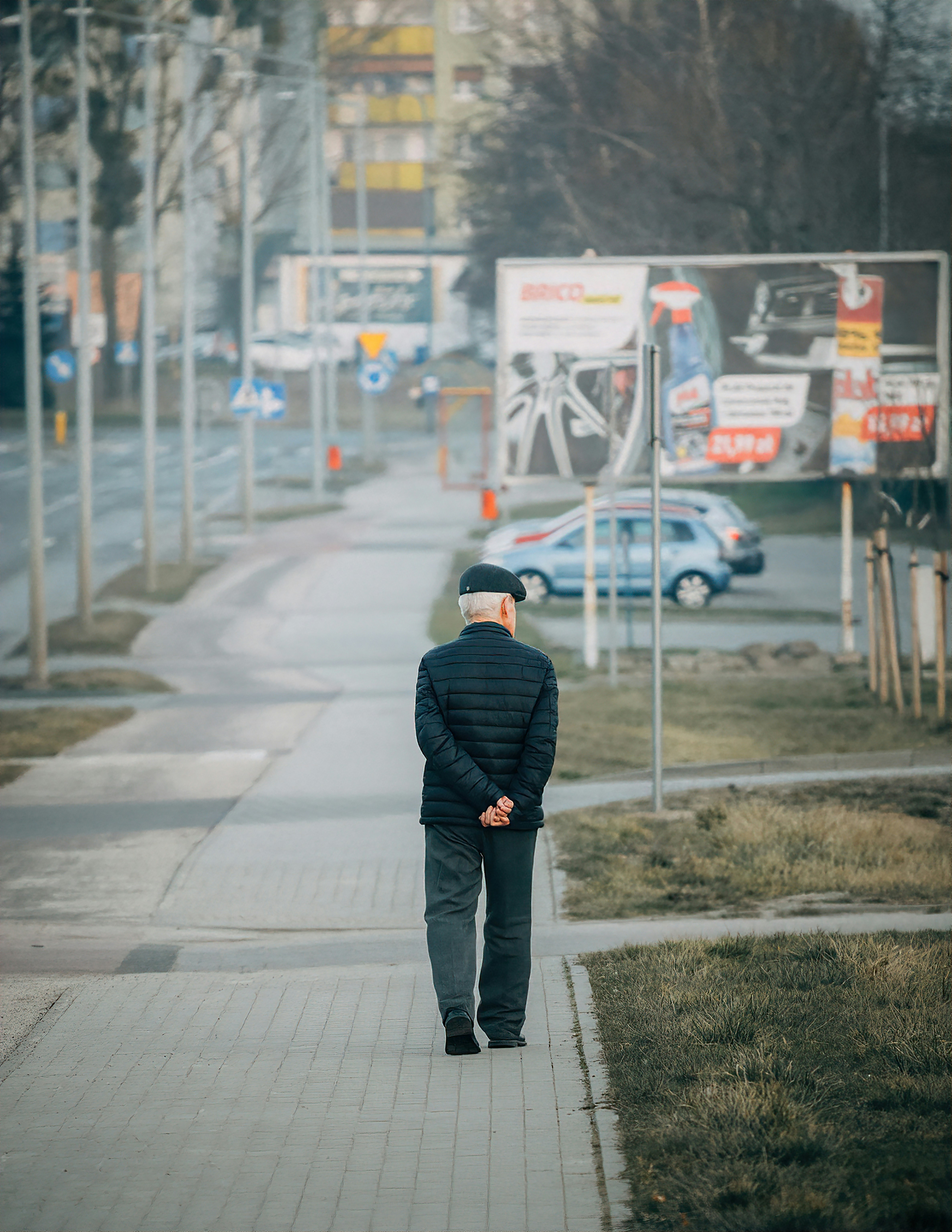 An elderly man walks along a city sidewalk.