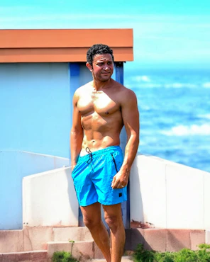 A muscular man stands by the ocean