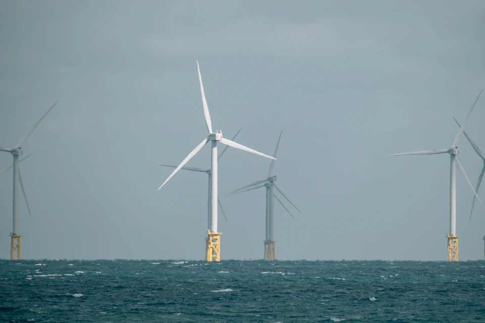 Six wind turbines stand on yellow poles near the ocean's surface with angled positions