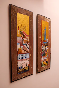 Two city paintings hang on a wall.