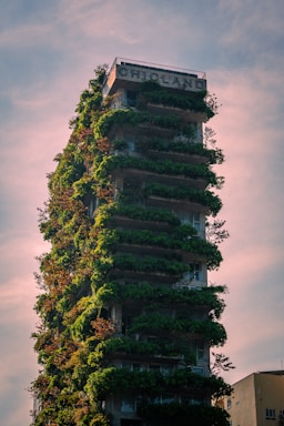 A green skyscraper is covered in plants.