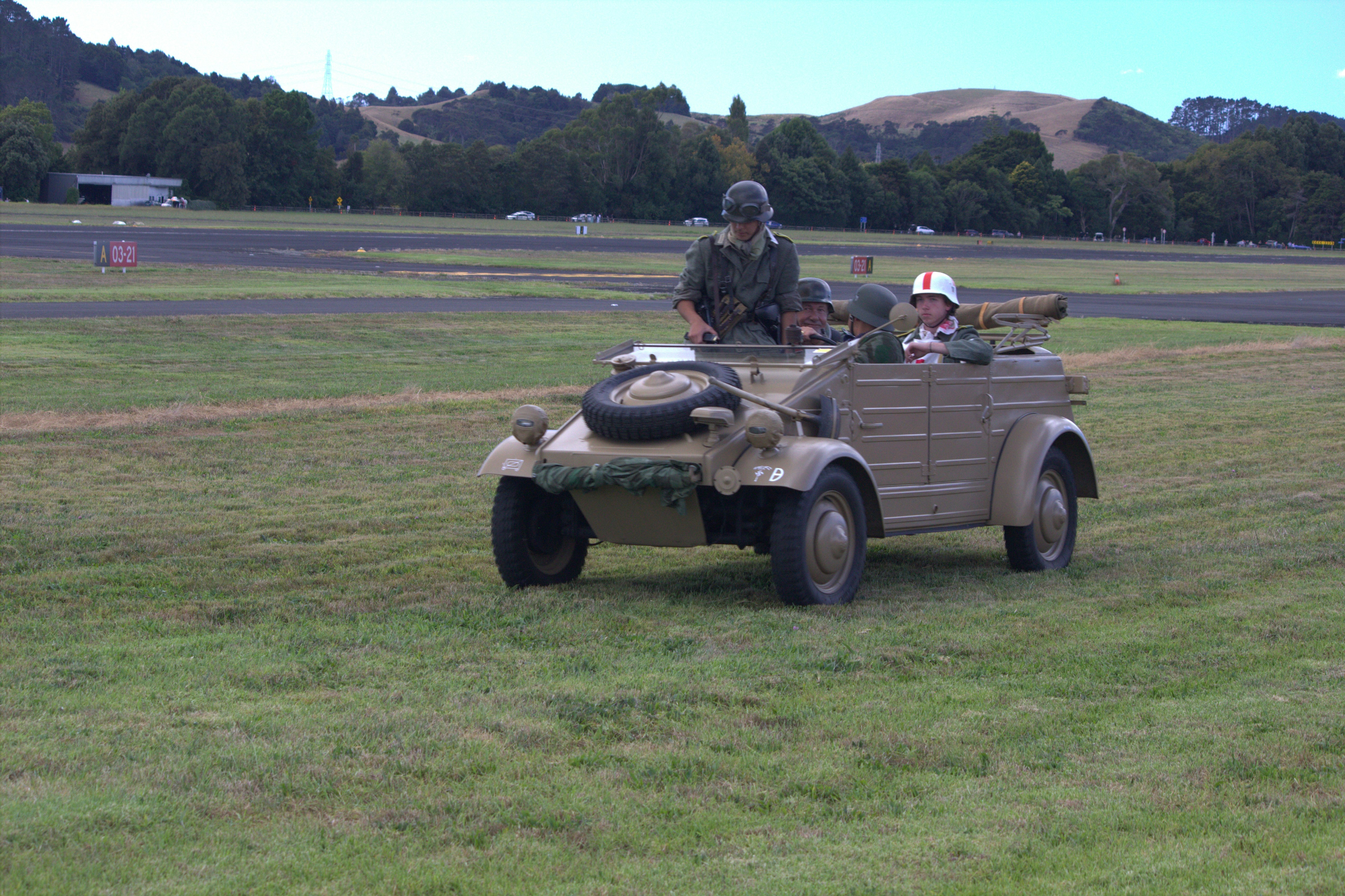 A military vehicle drives across a grass field.